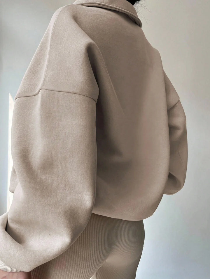 Close-up of a person wearing an oversized beige sweatshirt and beige ribbed pants against a plain background