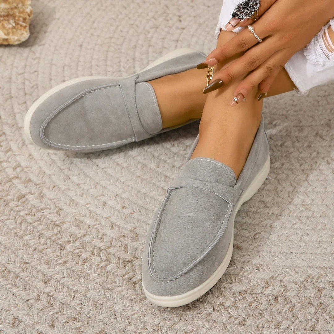 Close-up of women's feet wearing grey suede loafers on textured carpet with manicured nails and rings