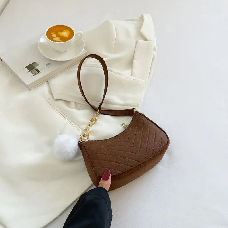 Brown quilted handbag with gold chain and white pompom on white blazer next to cup of latte with heart art