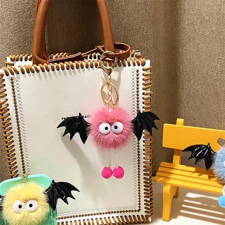 White leather handbag with brown handle and pink furry bat keychain with large eyes and black wings
