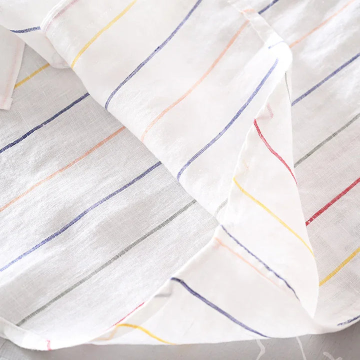 White fabric with colorful thin vertical stripes in red, yellow, blue, orange, and gray on a light surface