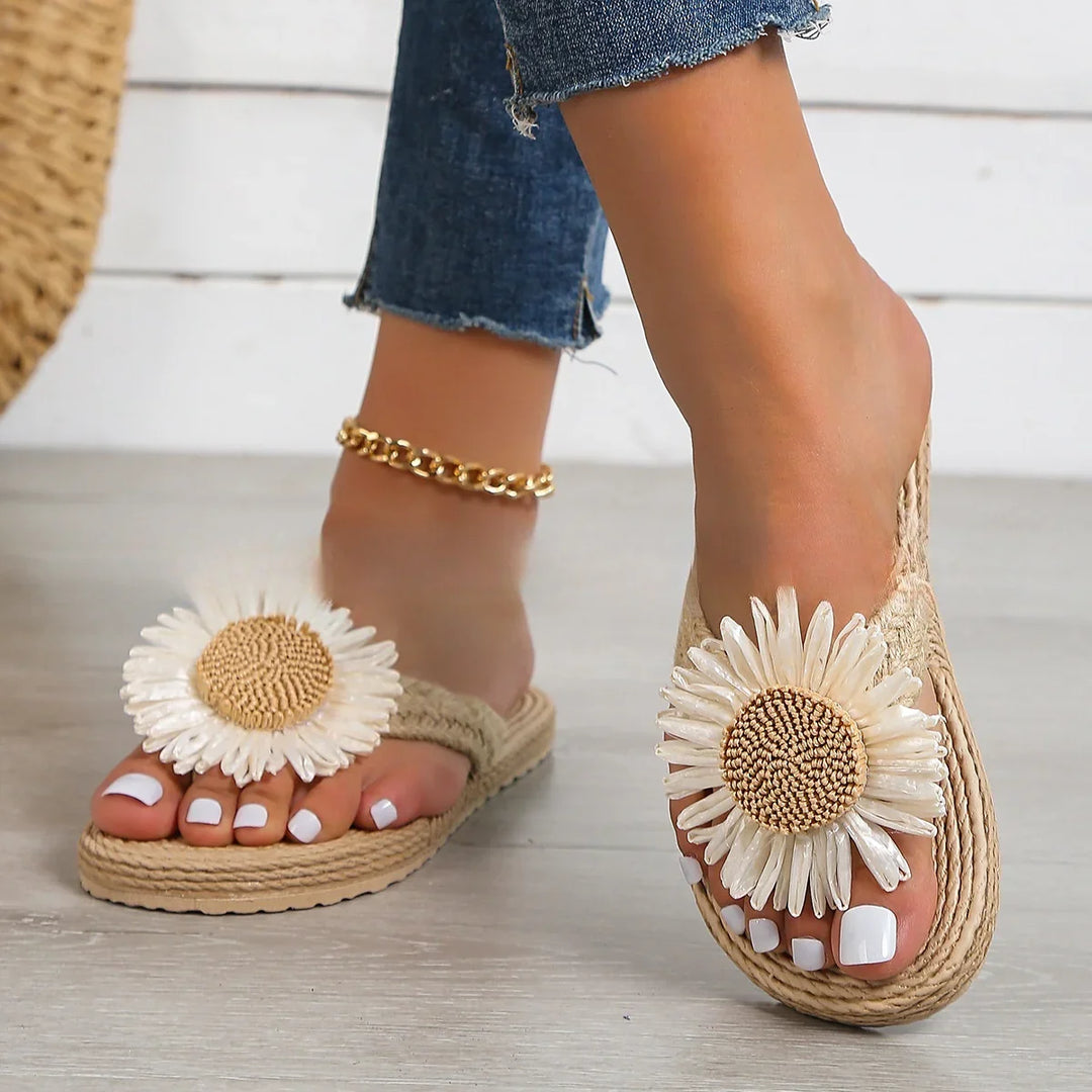 Woman wearing beige woven sandals with large daisy flower decoration and white pedicure