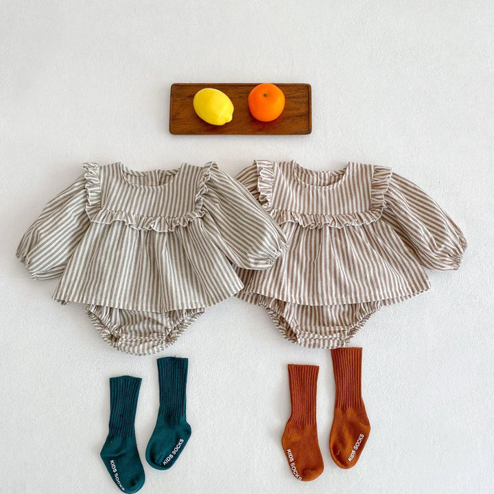 Two striped long-sleeve baby rompers with ruffle detailing paired with blue and orange kids socks, lemon and orange on wooden tray