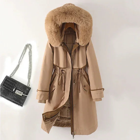 Beige winter coat with large fur hood and drawstring waist next to black textured handbag with silver chain