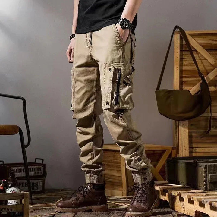 Man wearing beige cargo pants with zipper pocket and dark brown boots in rustic setting