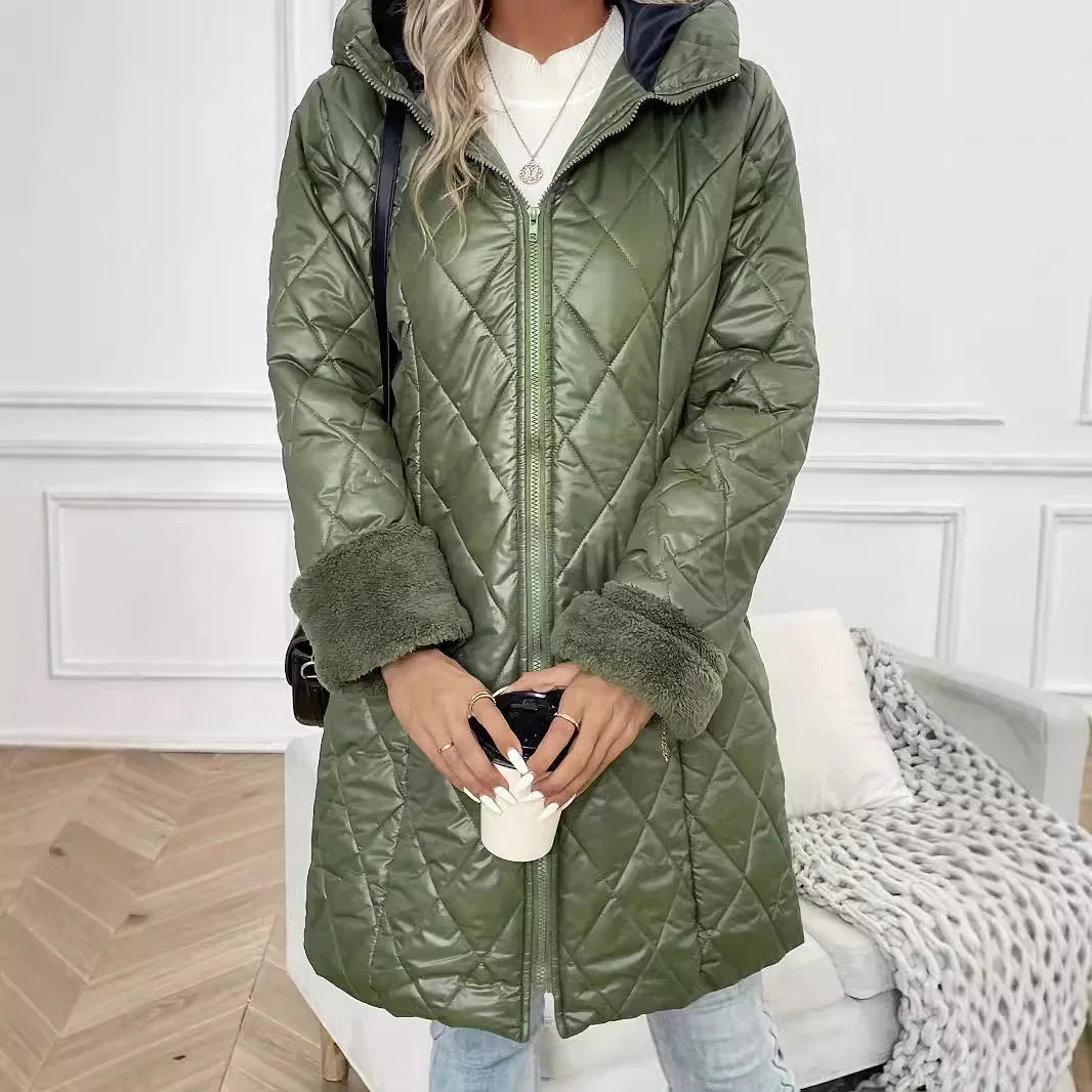 Woman wearing stylish olive green quilted coat with furry cuffs holding a white cup indoors