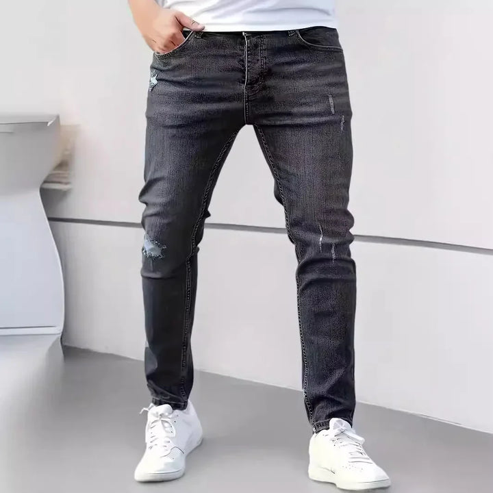 Man wearing slim fit distressed black jeans and white sneakers, standing indoors