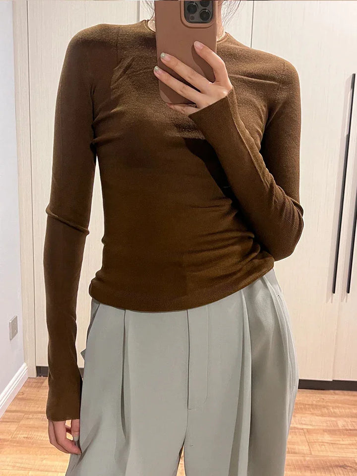 Person wearing a fitted brown long-sleeve top and high-waisted light gray pleated pants taking a mirror selfie indoors