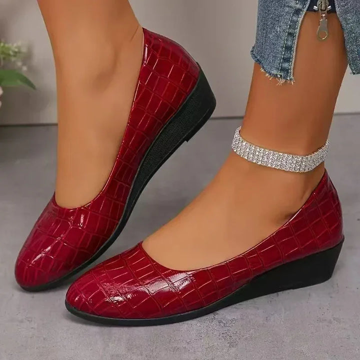 Close-up of feet wearing red crocodile pattern wedge shoes and a rhinestone ankle bracelet with cropped jeans