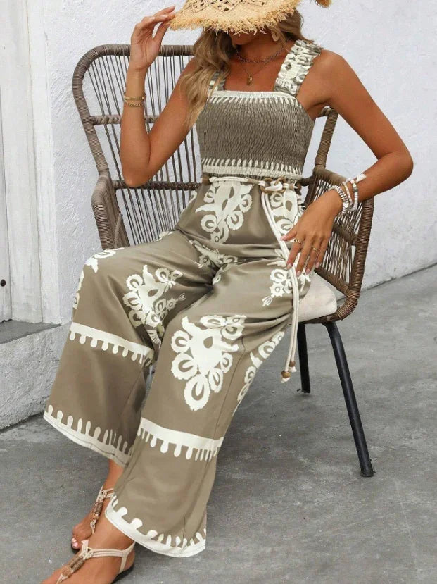 Woman wearing beige and white boho print wide-leg jumpsuit and straw hat, seated on rattan chair