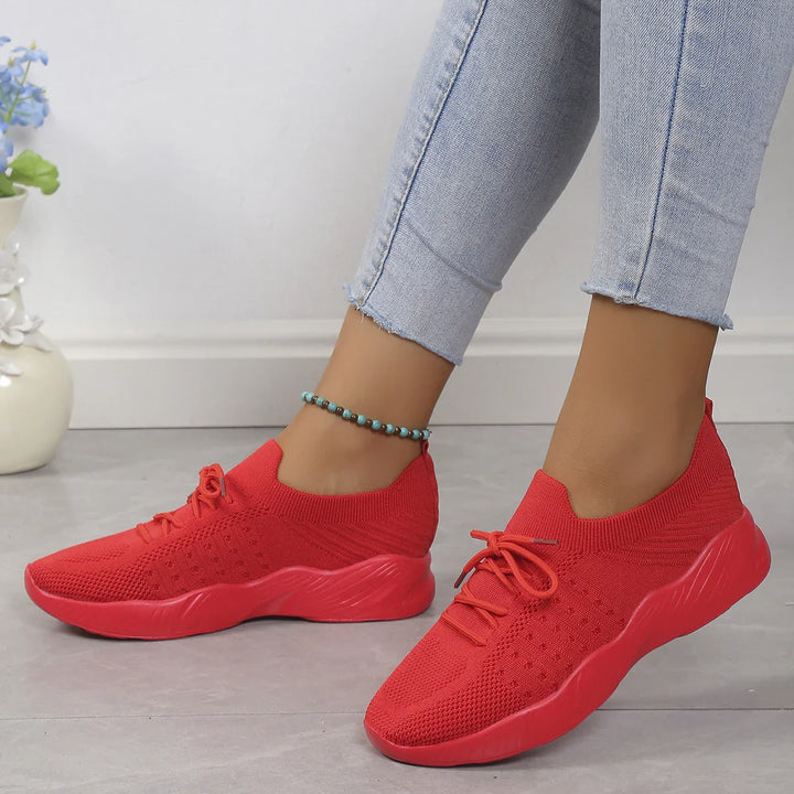 Close-up of feet wearing bright red knitted sneakers with thick soles and light blue jeans