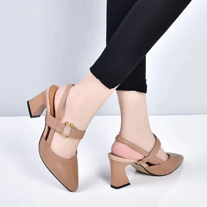Close-up of beige block heel slingback shoes with gold buckle worn with black pants on light background