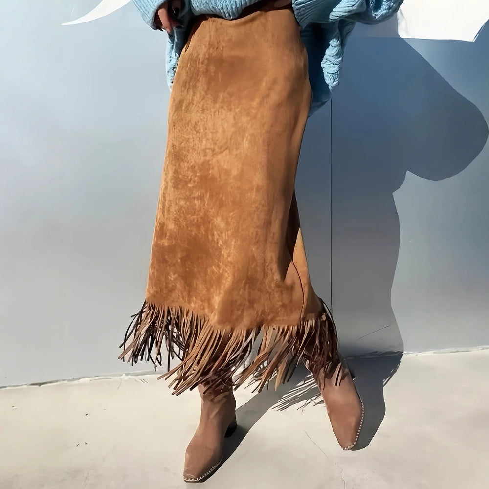 Woman wearing a suede brown fringe midi skirt and matching brown suede ankle boots against a plain background