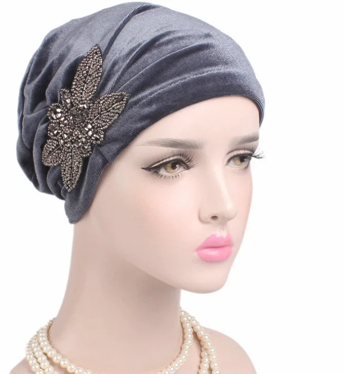 Mannequin wearing a gray velvet turban with a decorative jeweled flower and pearl necklace