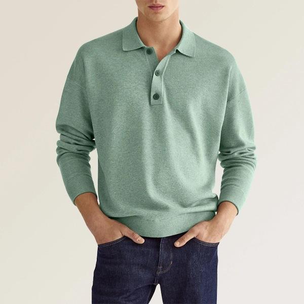 man wearing light green long-sleeve polo sweater and dark blue jeans with hands in pockets
