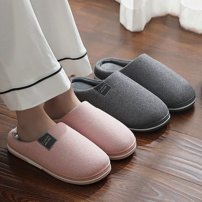 Pair of pink and grey cozy indoor slippers with herringbone pattern on wooden floor