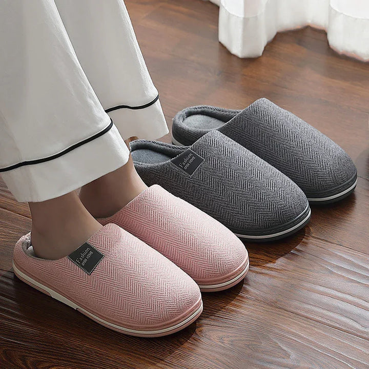 Pair of pink and grey cozy indoor slippers with herringbone pattern on wooden floor