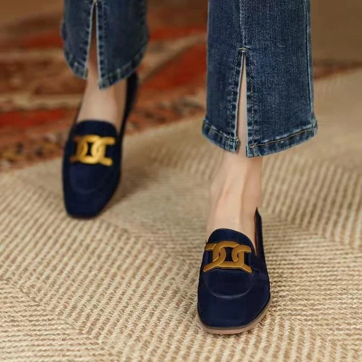 Navy blue suede loafers with gold chain detail worn with cropped split hem jeans on textured rug