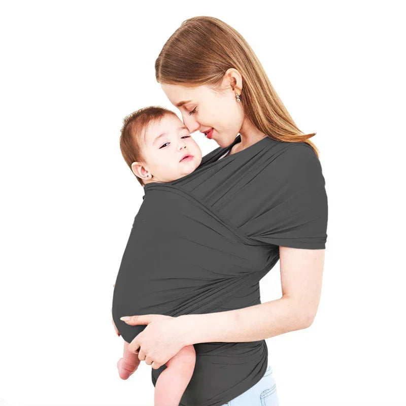Mother wearing black baby wrap carrier holding infant close against white background