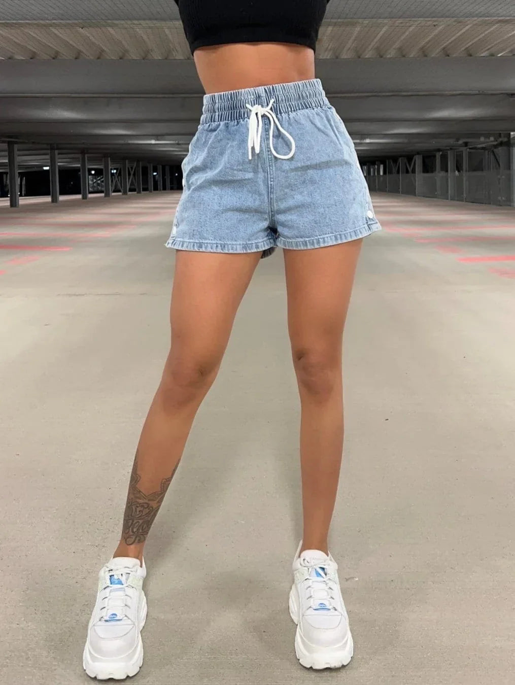 Woman wearing light blue denim shorts and white sneakers in an empty indoor parking garage