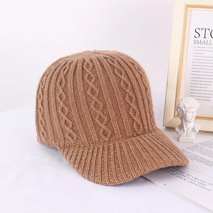 Brown knitted cable pattern baseball cap on white surface with framed art and small bust sculpture