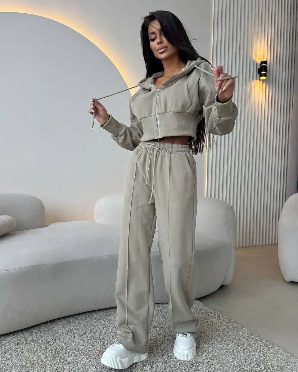 Woman in beige cropped hoodie and matching wide-leg pants with white platform sneakers in modern living room