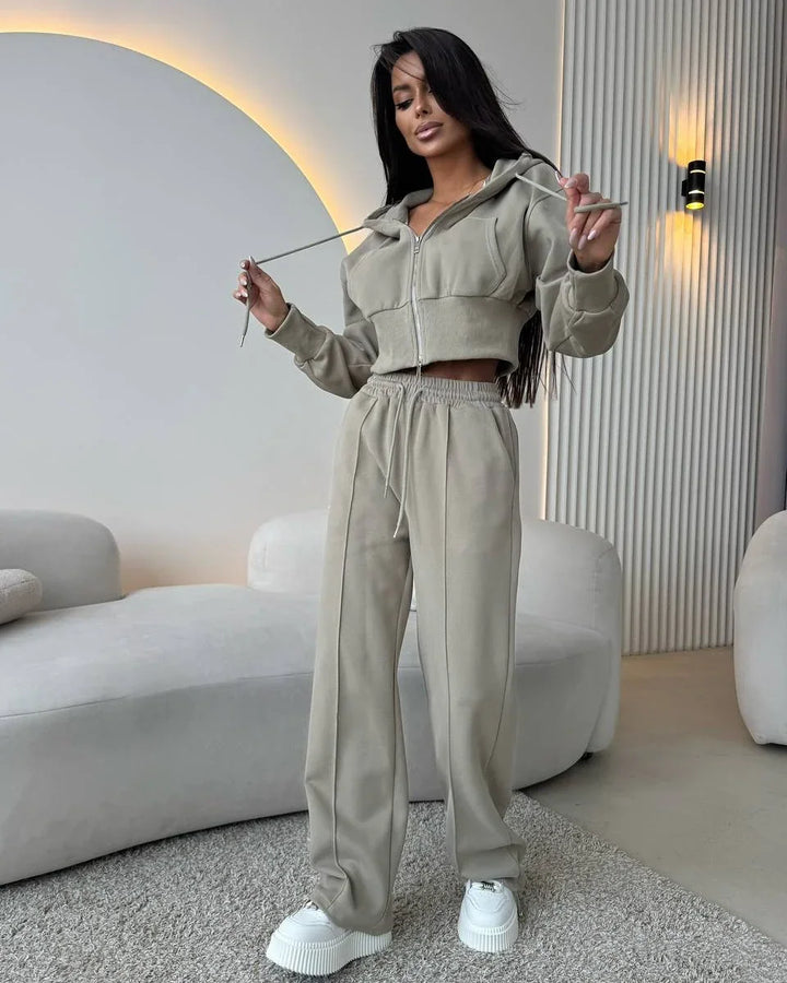 Woman in beige cropped hoodie and matching wide-leg pants with white platform sneakers in modern living room