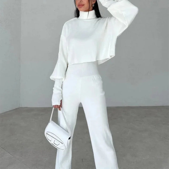 Woman wearing white turtleneck cropped sweater and high-waisted wide-leg pants holding white handbag