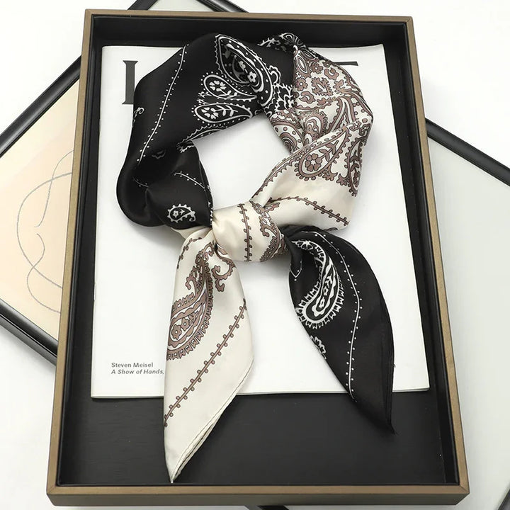Black and white paisley silk bandana scarf neatly tied and displayed in a black tray