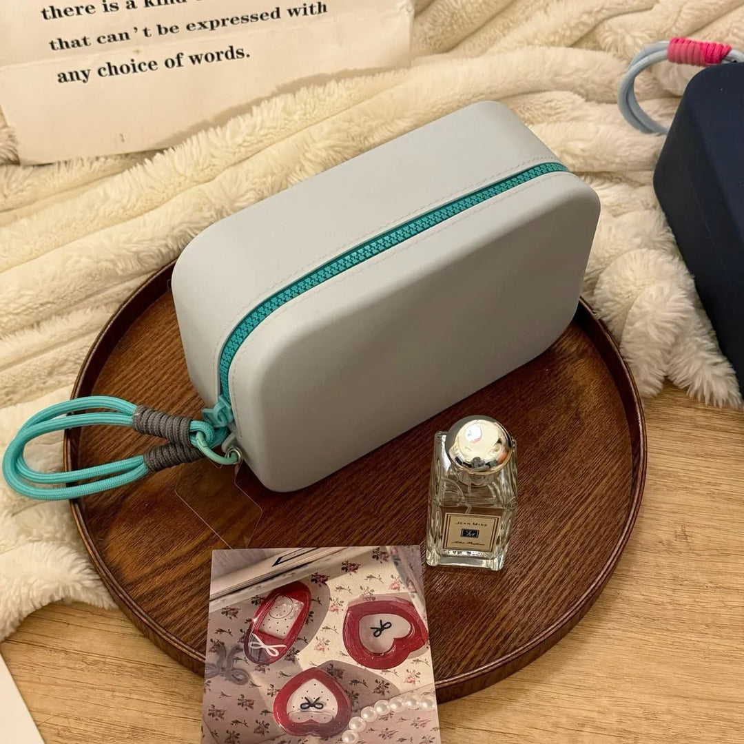 Minimalist gray rectangular pouch with teal zipper and loop on wooden tray with perfume bottle and photo card