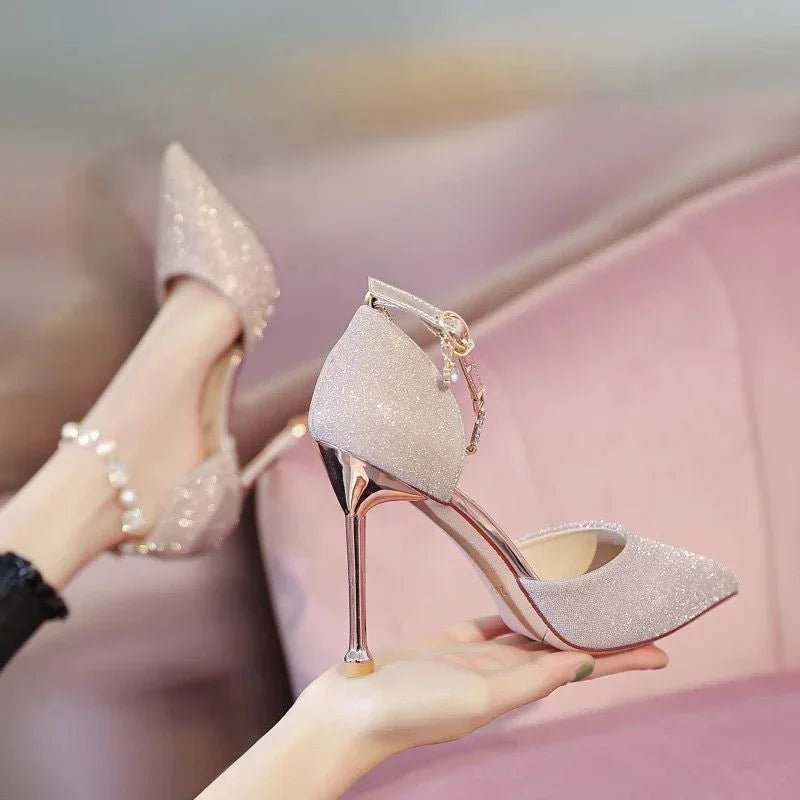 Elegant glittery pink high-heeled shoes with ankle strap and pearl detail on pink sofa