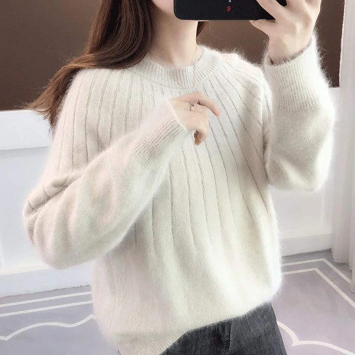 Woman wearing a soft, white ribbed knit sweater taking a mirror selfie indoors