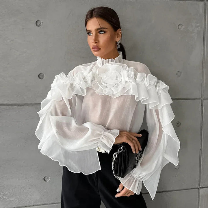 Woman wearing elegant white ruffled blouse with floral detail, holding black clutch bag, gray concrete wall background