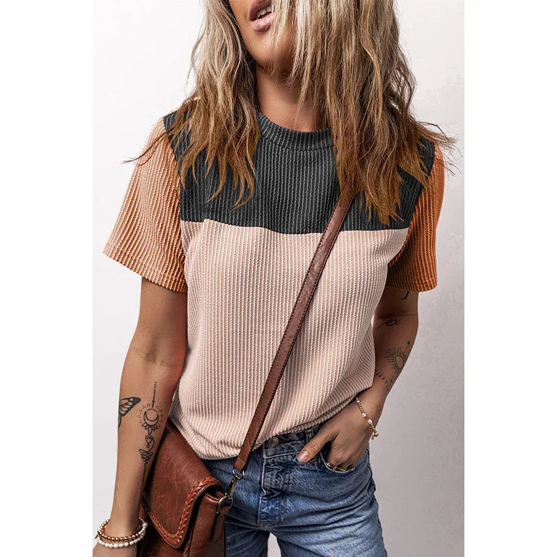 Woman wearing color-block textured short sleeve top with black, beige, and rust tones, paired with denim jeans and brown leather crossbody bag