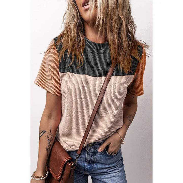 Woman wearing color-block textured short sleeve top with black, beige, and rust tones, paired with denim jeans and brown leather crossbody bag
