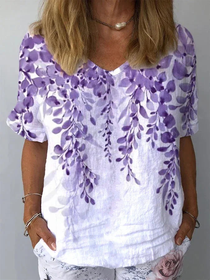 Woman wearing white short-sleeve V-neck shirt with purple floral print and white pants with floral design