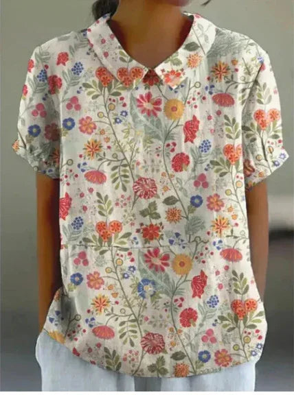 Woman wearing a short-sleeve floral print blouse with a peter pan collar, white background