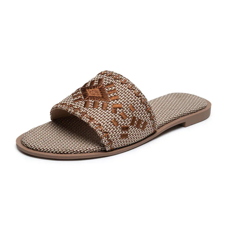 Brown woven slide sandal with geometric embroidery and flat sole on white background
