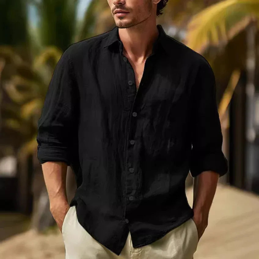 Man wearing black long-sleeve linen shirt and light pants outdoors with palm trees background