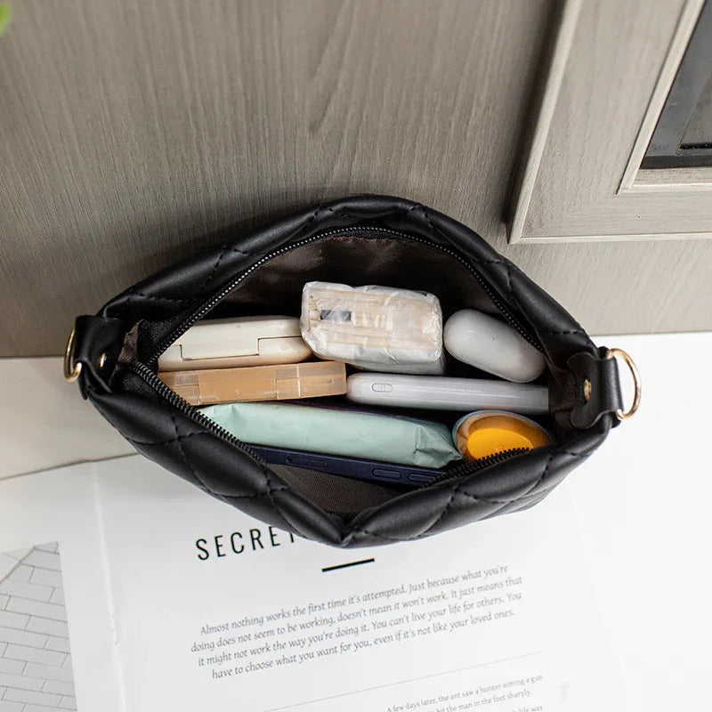 Top view of a black quilted purse filled with cosmetics and a wireless earbud case