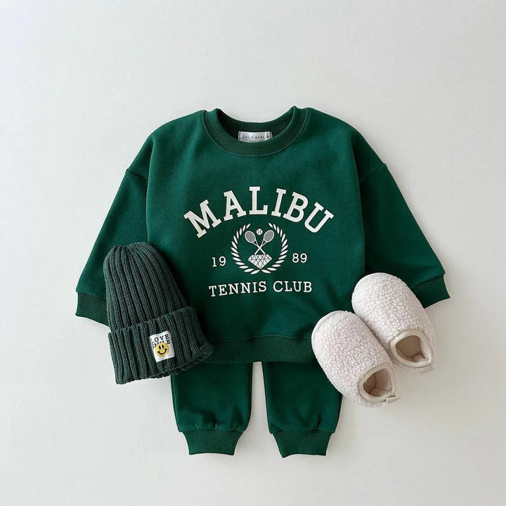 Dark green children's sweat set with Malibu Tennis Club print, matching pants, knit hat, and white fuzzy slippers