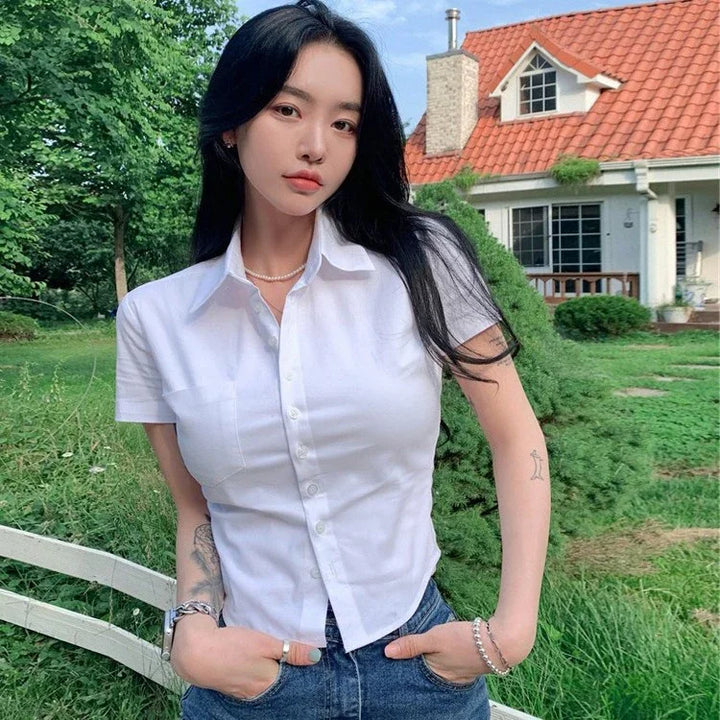 Young woman with long black hair wearing white button-up shirt and jeans standing outdoors in front of house with red roof