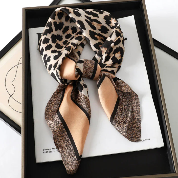 Silky leopard print and beige patterned scarf neatly tied in a black frame with minimalist background