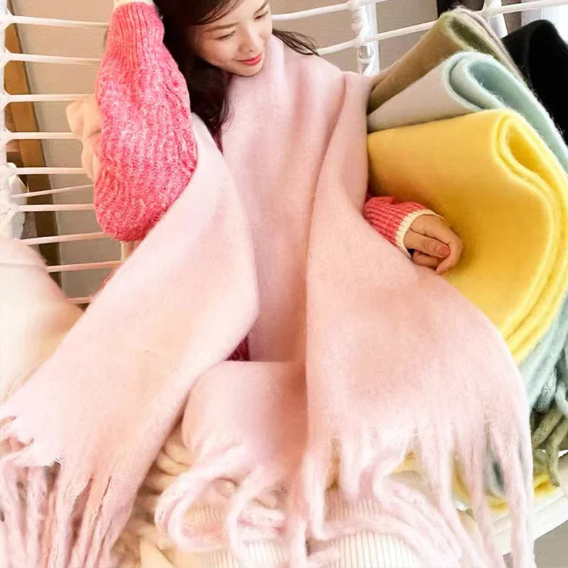 Woman wrapped in soft pastel pink scarf sitting next to rolled colorful wool scarves