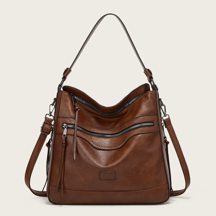 Brown leather shoulder bag with front zipper pocket and adjustable strap on beige background