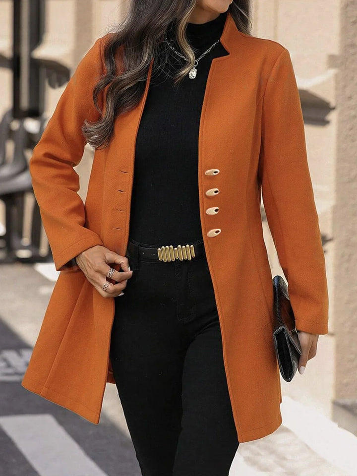 Woman wearing stylish orange coat with black turtleneck and black pants outdoors, holding black clutch