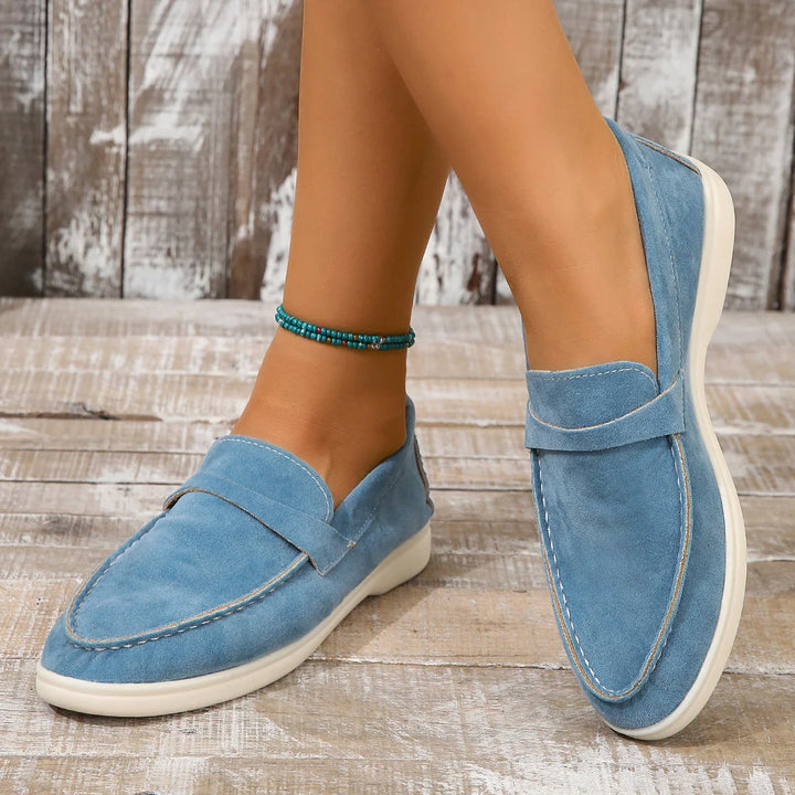 Women's light blue suede loafers with white soles worn with a turquoise beaded ankle bracelet