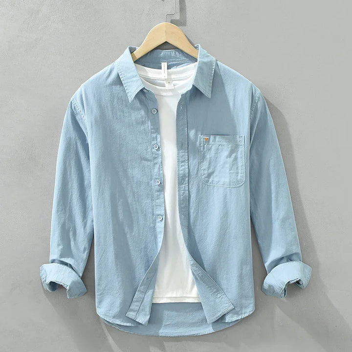 Light blue casual button-up shirt over white t-shirt on wooden hanger against gray wall