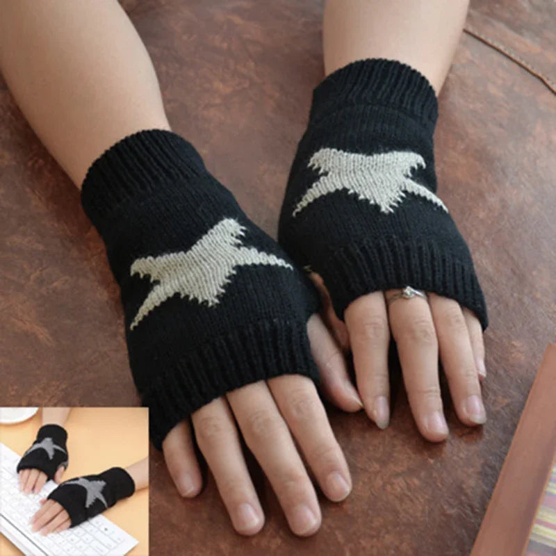 Hands wearing black knit fingerless gloves with white bird design on wooden surface