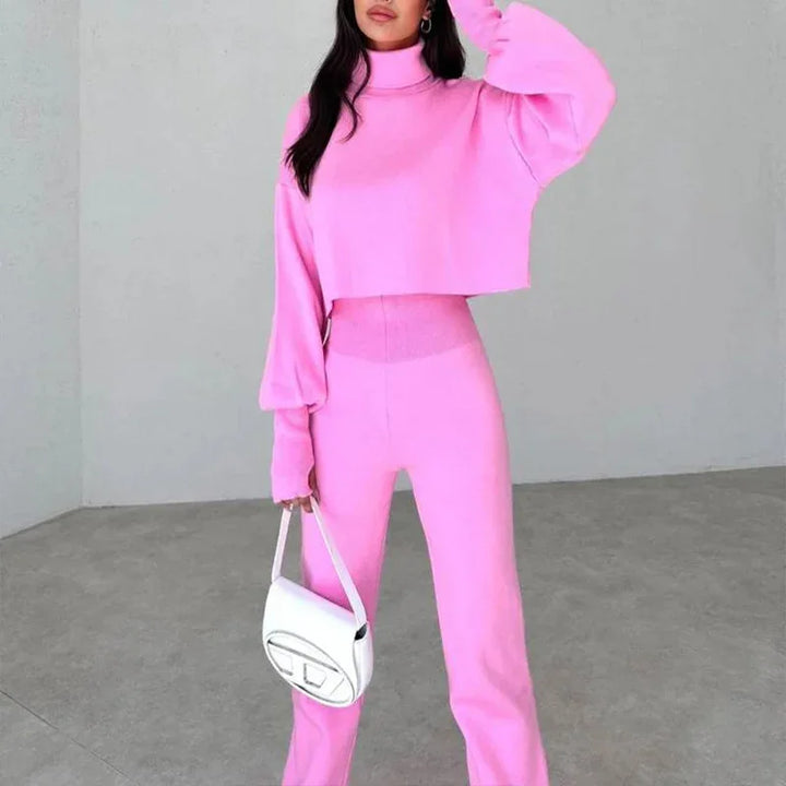 Woman wearing pink matching turtleneck crop top and high-waisted pants holding a white handbag